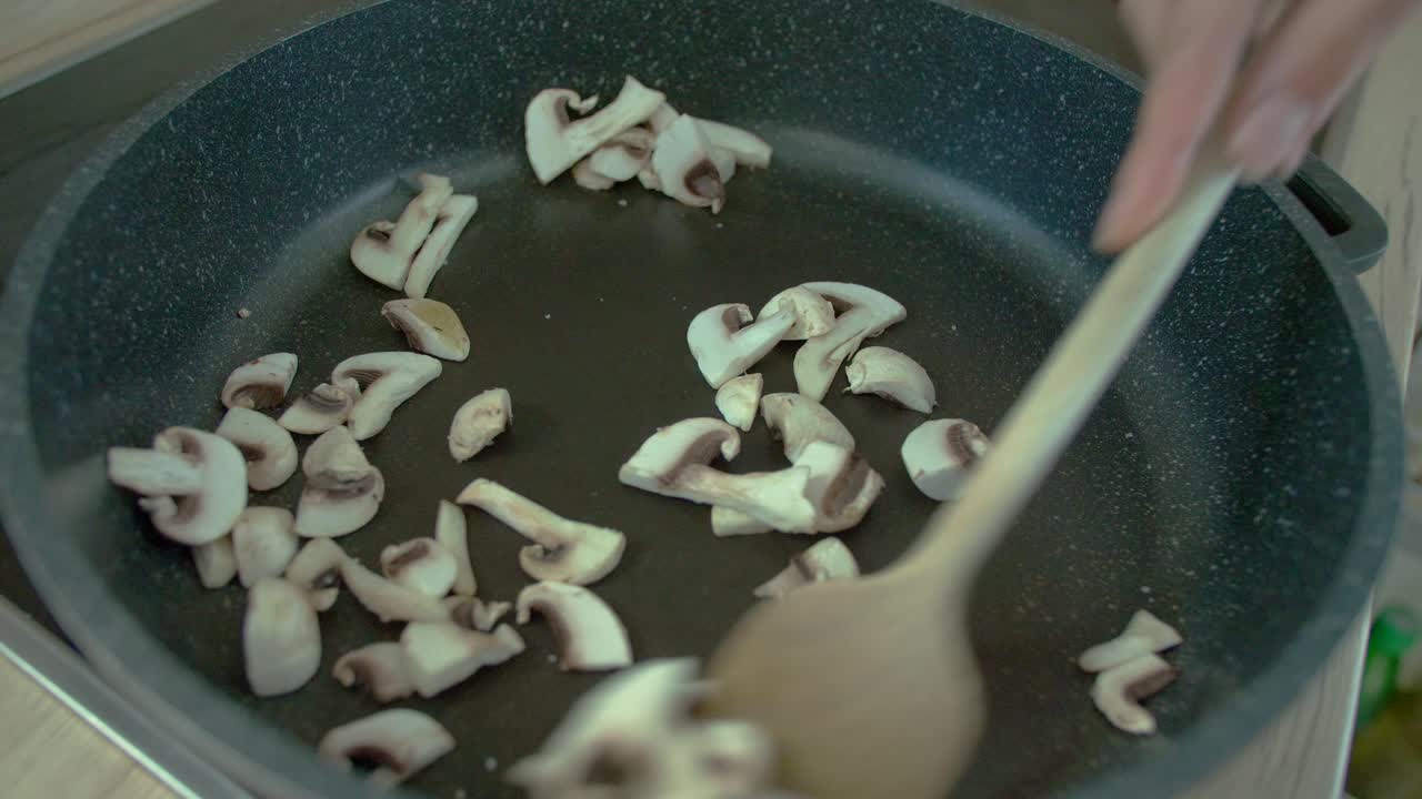 Top view of female stir frying mushrooms in pan
