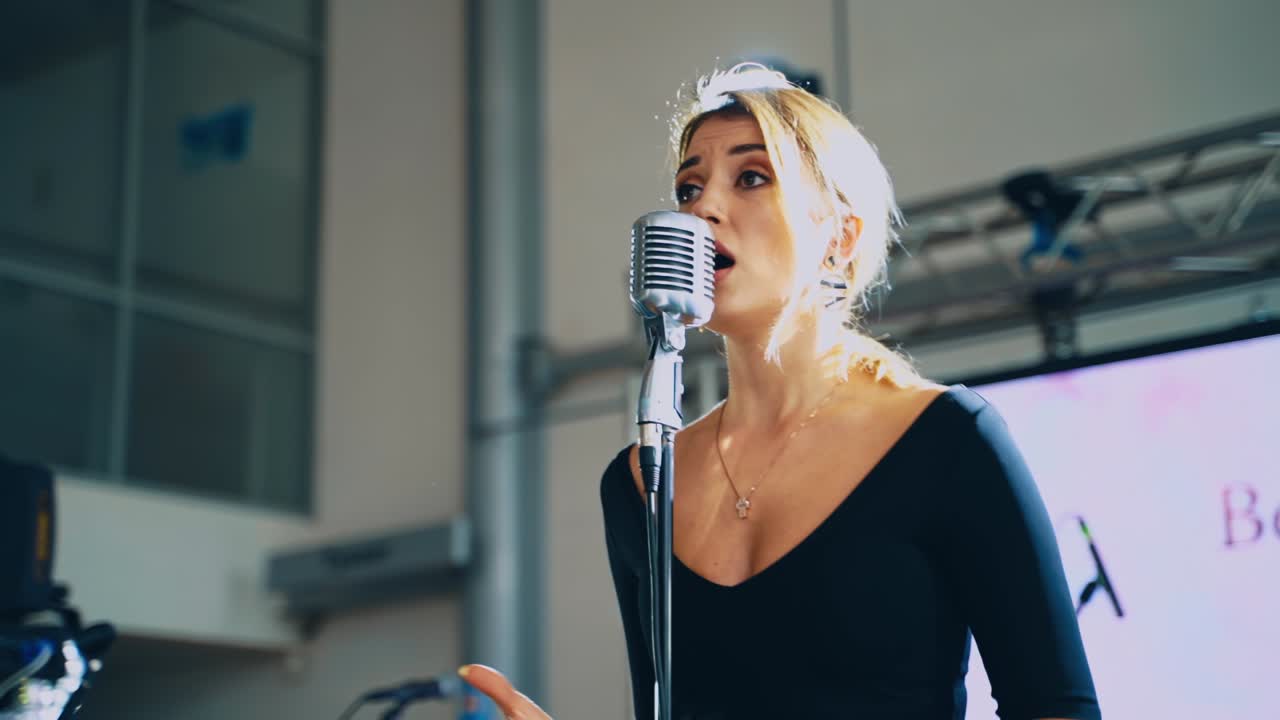 Portrait of a beautiful young singer. Blonde woman standing on the stage and singing into the microphone. Slow motion.