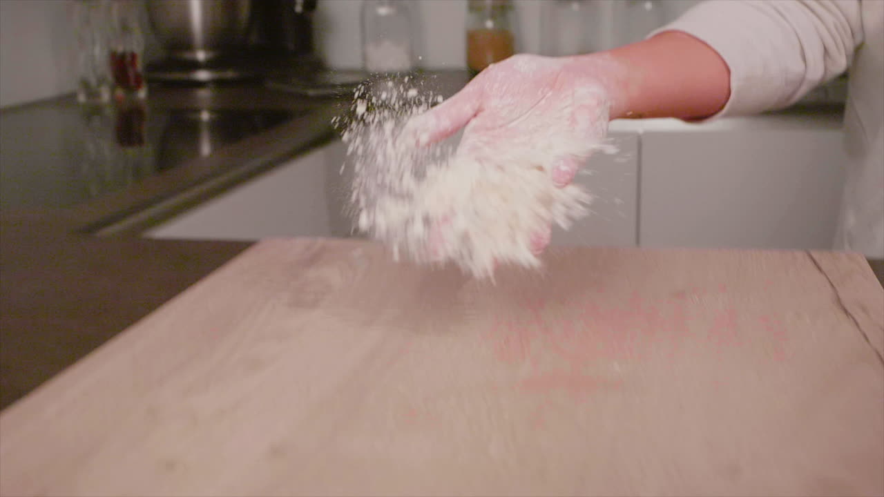 woman's hand throws flour on the table in the kitchen close up, slow motion