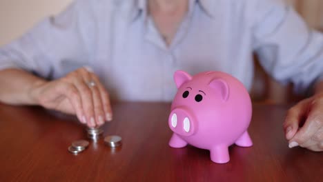 mujer poniendo monedas en la alcancía rosa en la mesa