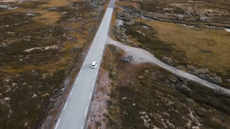 4k aerial: flying above white vw golf, car driving along empty countryside. people traveling, road trip through beautiful mountain scenery in sunny summer
