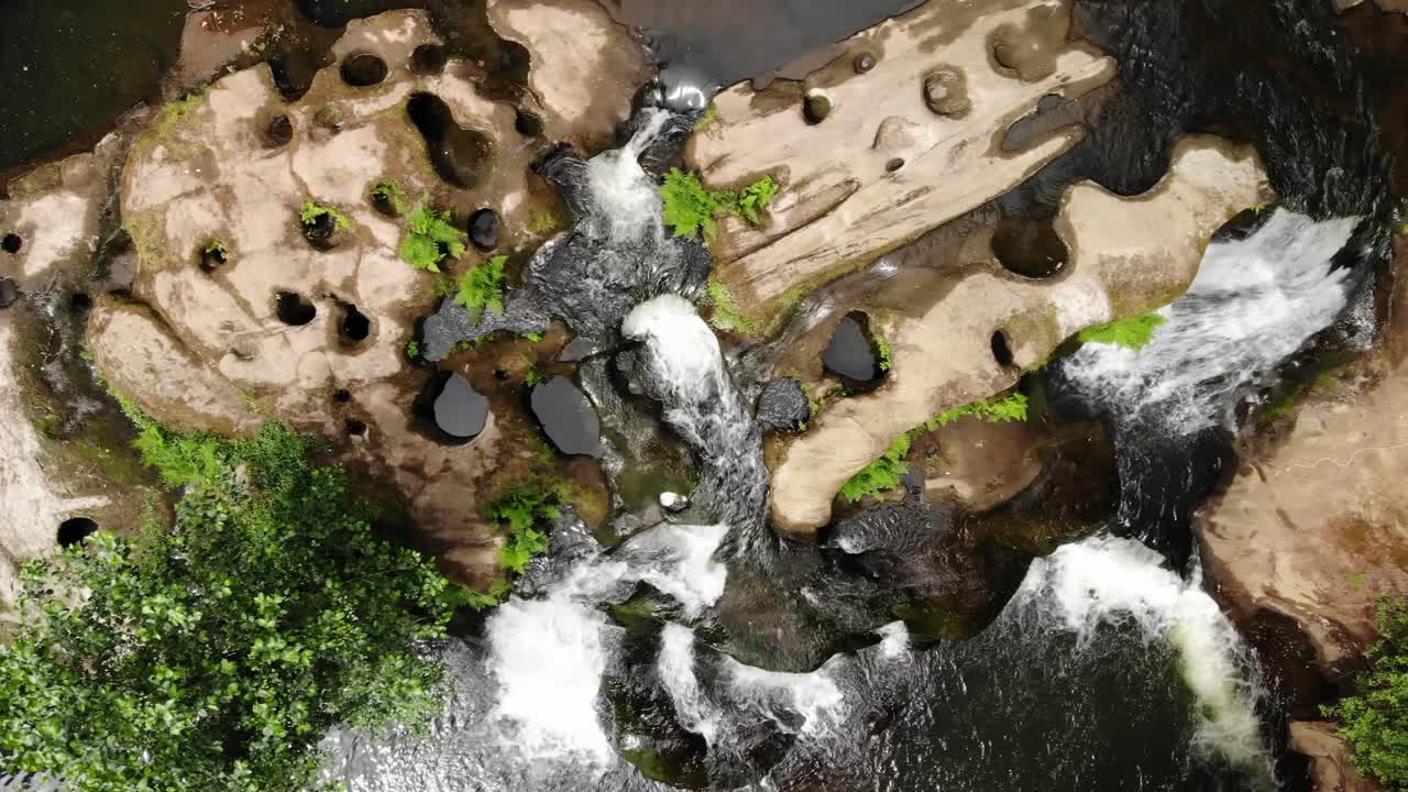 Luftfoto oppefra af naturligt skovlandskab med stenet flodstrøm og vandfald.