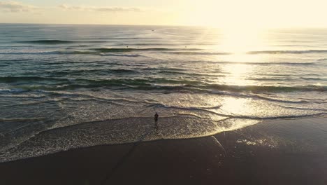 Aerial-view-of-Man-fishing-on-the-beach-shore-with-surfers-and-boats-out-on-a-reef-in-the-background-at-sunrise-in-Southport-Gold-Coast-QLD-Australia