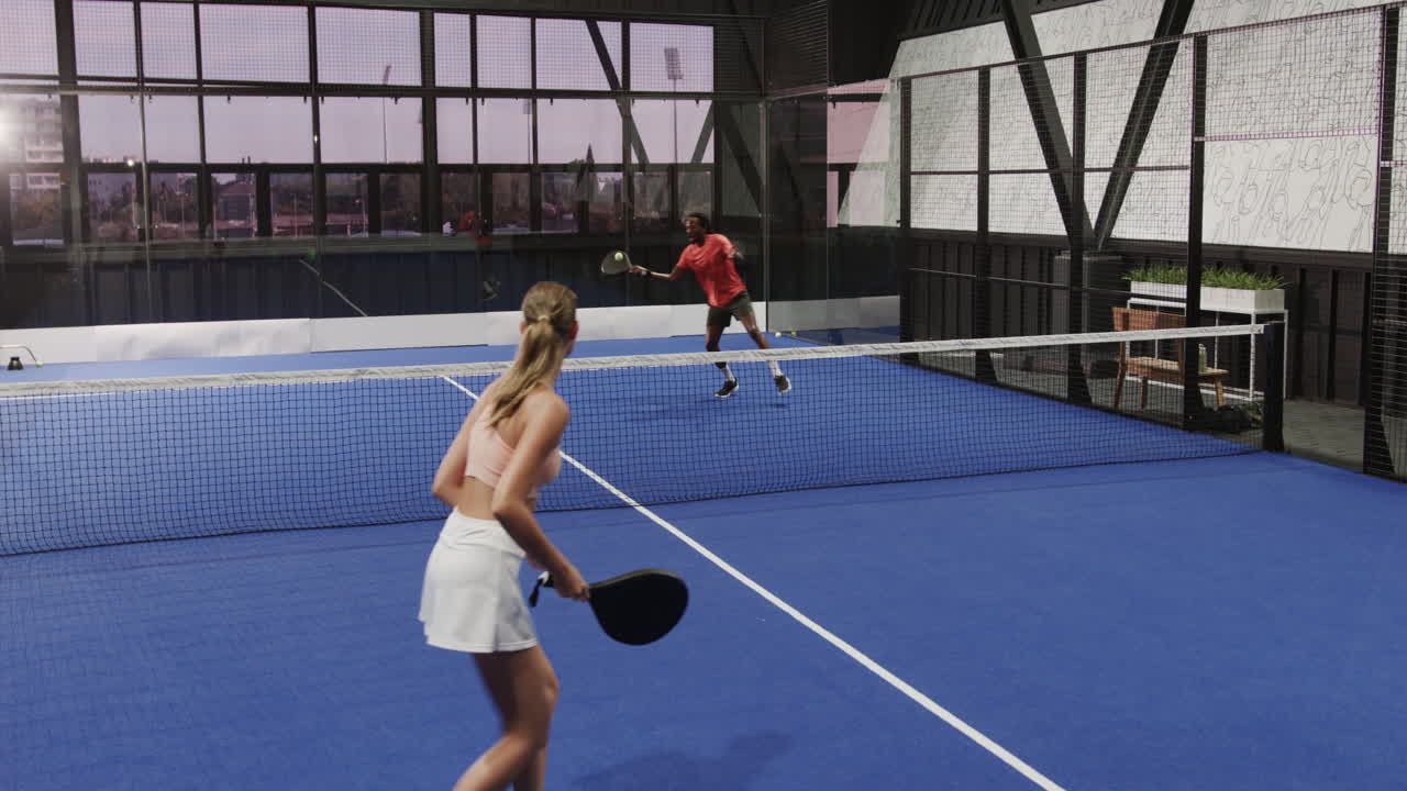 Two diverse athletes playing padel tennis on indoor court, focusing on intense rally