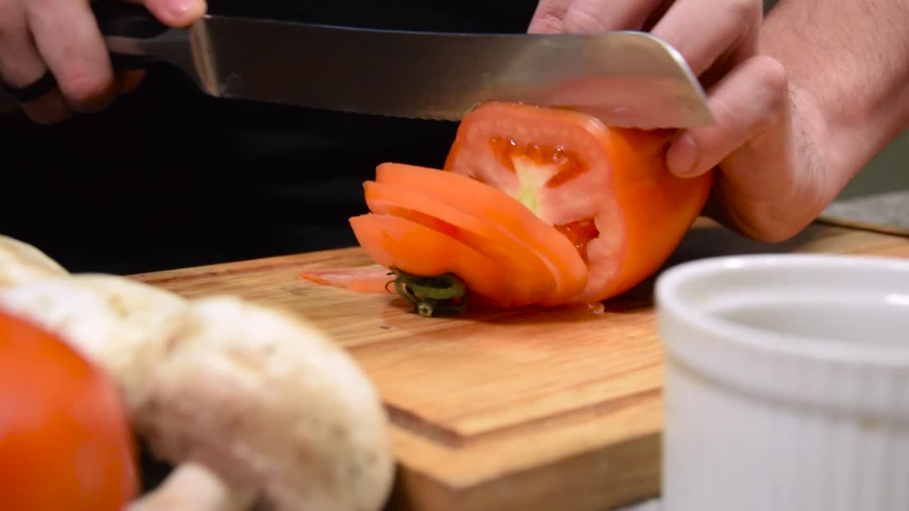 primer plano de un chef cortando un tomate en una mesa decorada con verduras