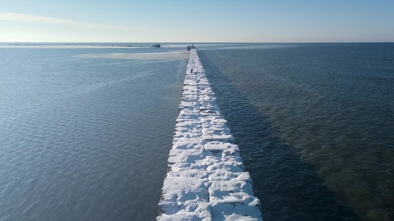 vista aérea de nieve y hielo cubierto muelle de hormigón en el tranquilo mar báltico, puerto de liepaja en un soleado día de invierno, disparo de drone de gran ángulo moviéndose lentamente hacia adelante