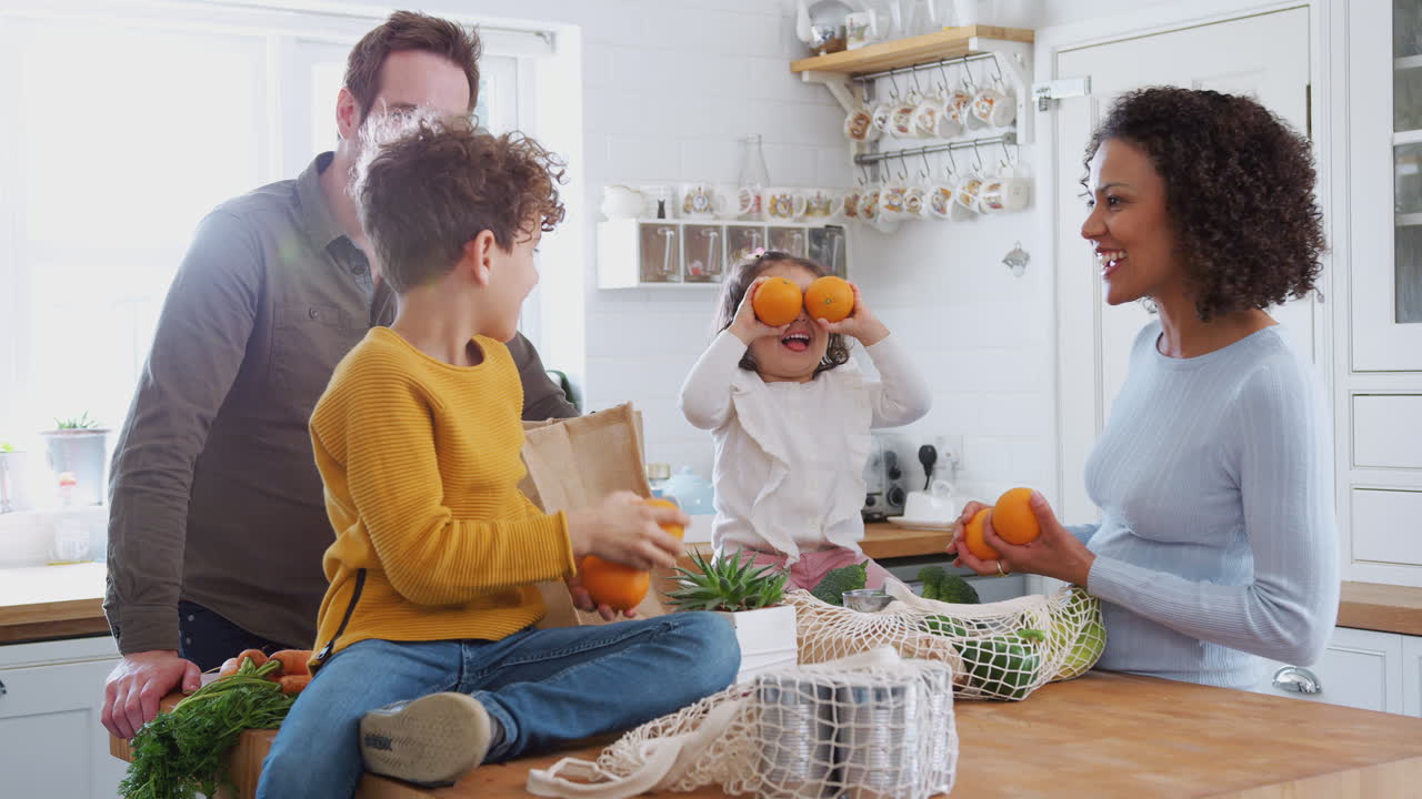Família voltando para casa de uma viagem de compras usando sacos de plástico livres Desembalando compras na cozinha