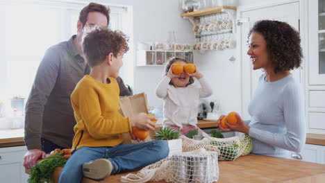 família voltando para casa de uma viagem de compras usando sacos de plástico livres desempacotando mantimentos na cozinha