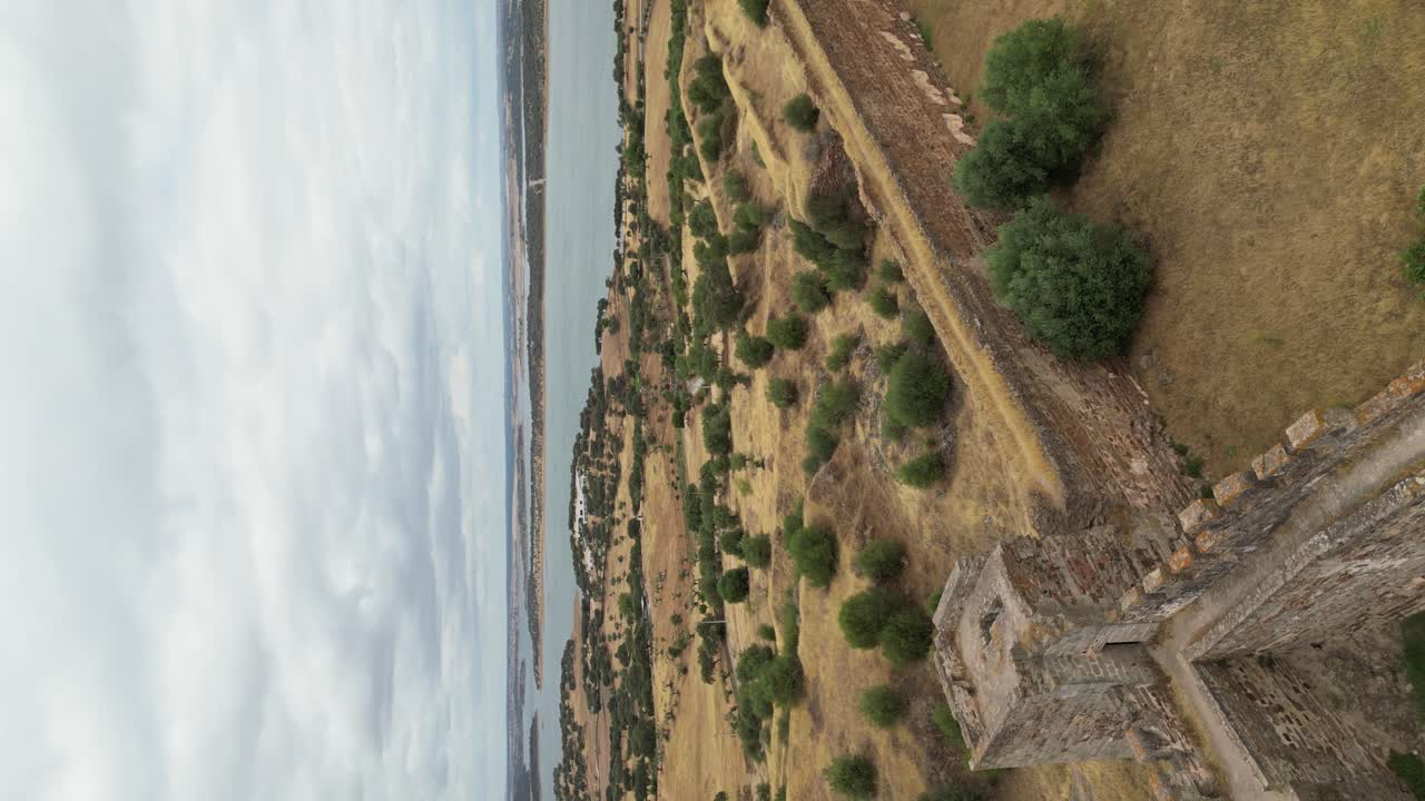 video vertical, sobrevuelo de drones muros de piedra del castillo de mourão hacia el lago alqueva, alentejo