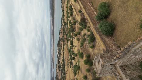 Video-Vertical,-Sobrevuelo-De-Drones-Muros-De-Piedra-Del-Castillo-De-Mourão-Hacia-El-Lago-Alqueva,-Alentejo