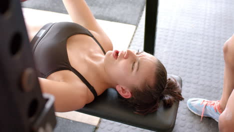 Mujer-Birracial-Determinada-E-Inalterada-Entrenando-Con-Pesas-En-El-Banco-Del-Gimnasio-Presionando-La-Barra,-En-Cámara-Lenta