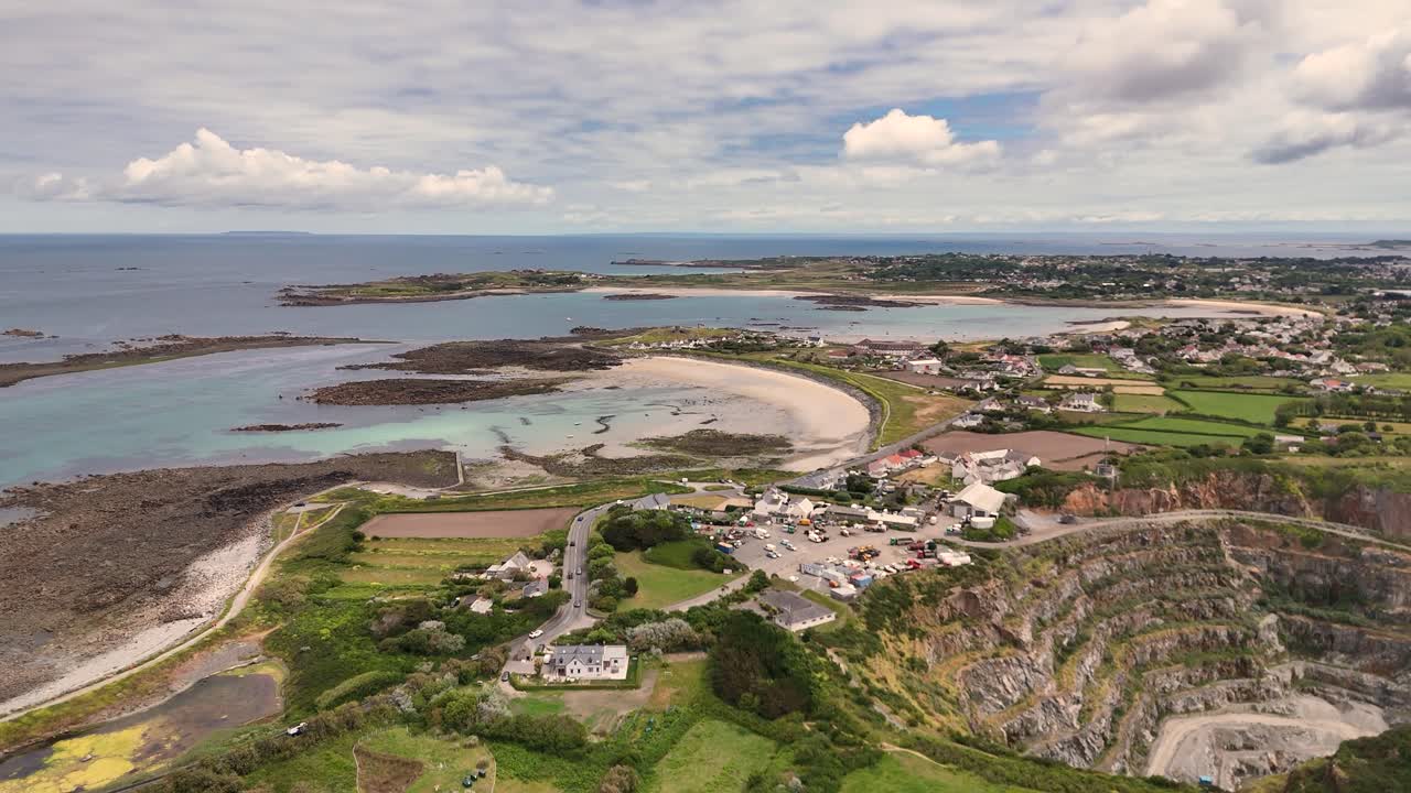 Guernsey.High drone flight over fields,derelict greenhouses, Les Vardes Quarry and golden beaches on West Coast on bright day