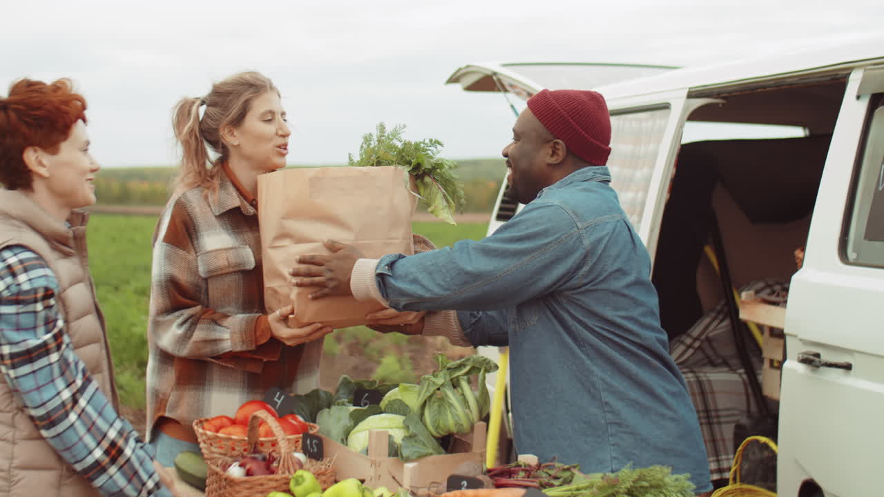 mujeres caucásicas comprando verduras frescas de un granjero negro