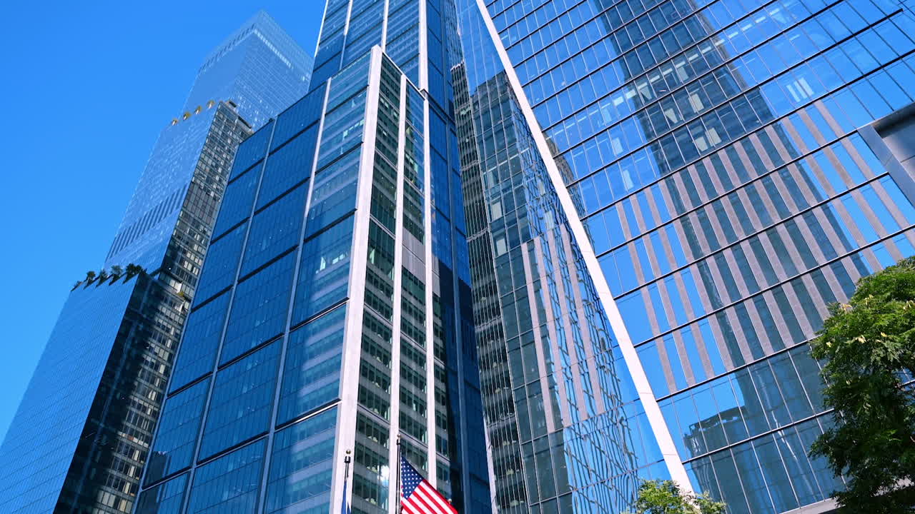 New York, USA, 5 August 2025: Three flags flap in the wind near the glass buildings. Looking the modern high-rises of New York from low-angle perspective
