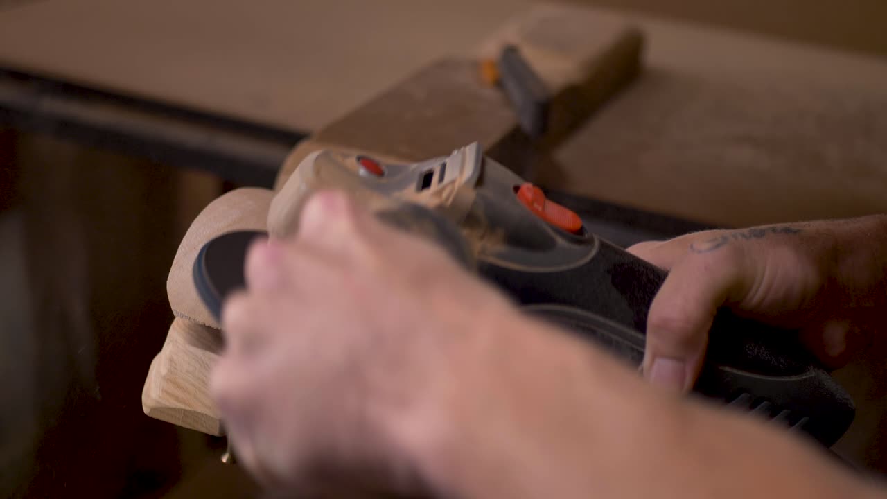 Slow motion close-up man using orbital grinder machinery tool with clamp to sand back and shape hardwood climbing block holds in indoor workshop DIY home shed Australia carpentry hobby industry power