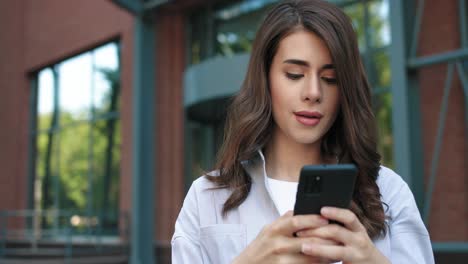 mujer estudiante caucásica usando un teléfono inteligente en la calle