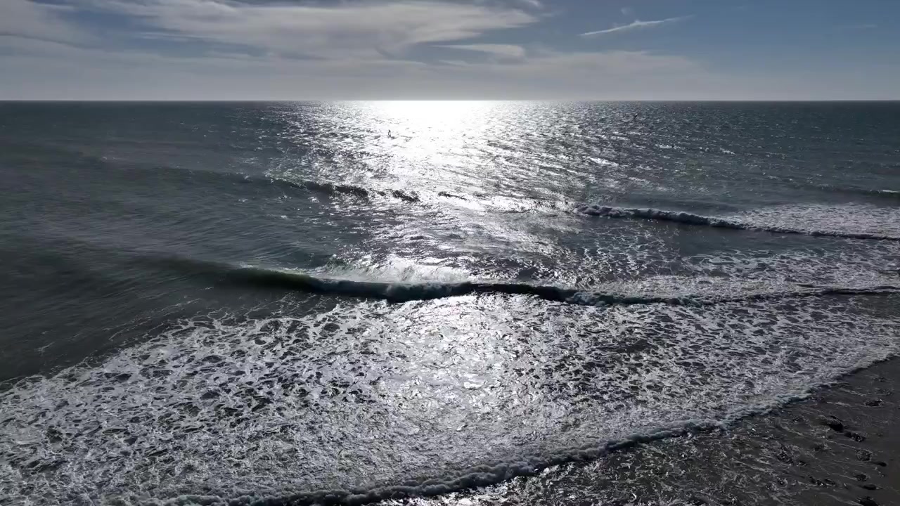 Vista aerea con drone del luccichio del sole sull'Oceano Atlantico vicino a Dakhla, Marocco, con onde dolci che creano un paesaggio marino costiero pacifico e cinematografico