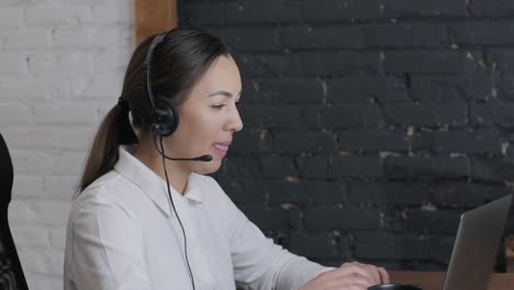 smiling woman call centre operator, customer support agent wears headset consults client online, typing on laptop, talk in internet computer chat, helpline operator secretary make conference video call