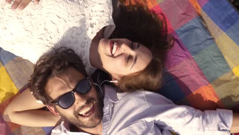 feliz y encantadora pareja joven acostada en una manta de colores en el parque escuchando música en el teléfono inteligente con auriculares romántico con gafas de sol de guitarra hermosa chica atractiva vista superior cámara giratoria en cámara lenta