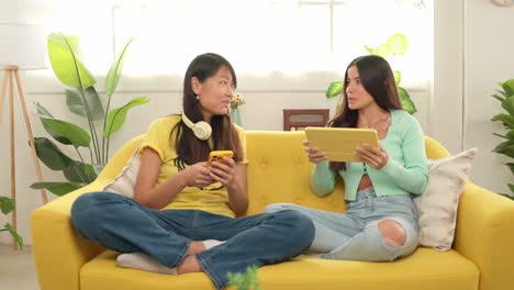 Two women relaxing on a yellow couch with technology