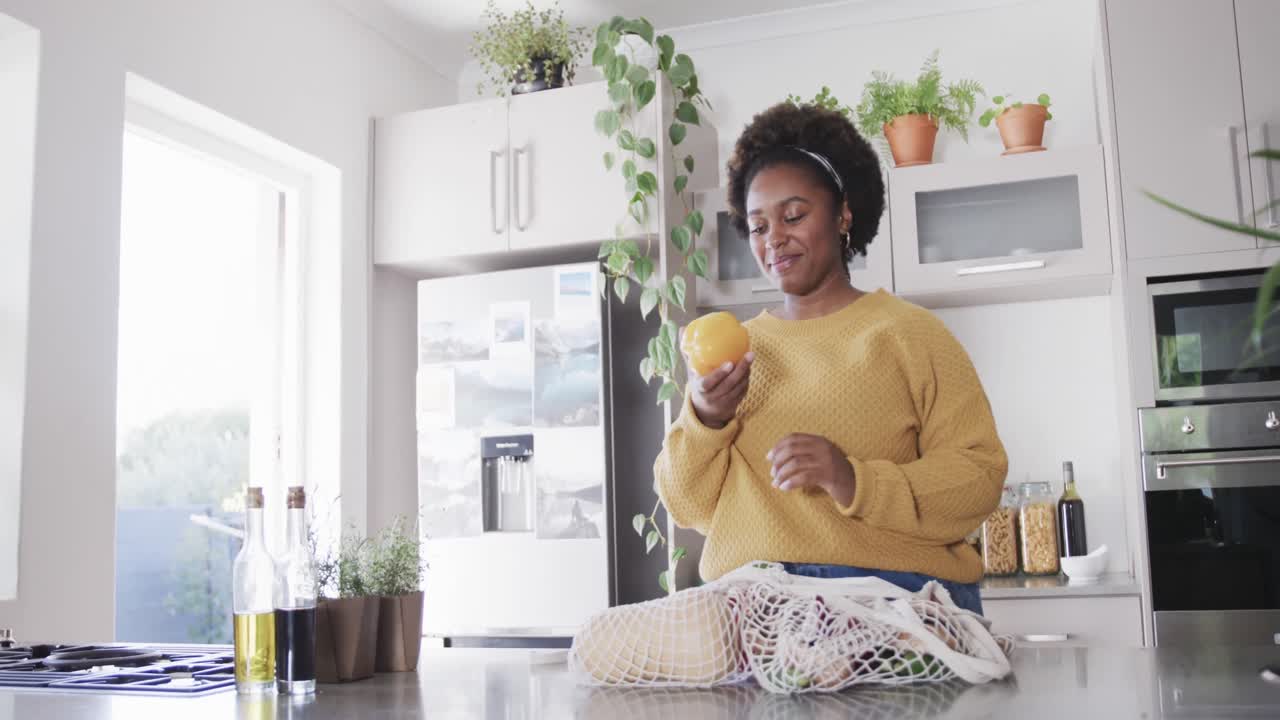 feliz mujer afroamericana desempaquetando y oliendo comestibles en la cocina, en cámara lenta