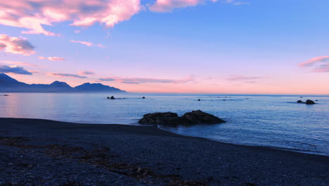 Drone-shot-of-sea-with-snow-capped-mountain-background-and-orange-sky