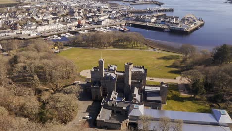 drone tilt-shot revealing the town of stornoway, the lews castle and the landscape beyond it on a sunny day on the isle of lewis, outer hebrides of scotland, united kingdom