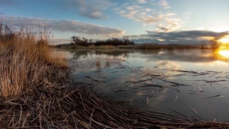 Wolken-Ziehen-Schnell-über-Den-Himmel-Und-Werden-Von-Der-Oberfläche-Eines-Sees-Reflektiert,-Während-Die-Sonne-In-Diesem-Zeitraffer-Aufgeht-–-Statischer-Weitwinkel