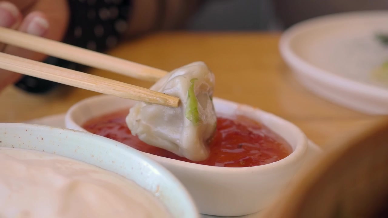 Dipping a Steamed Dumpling into Red Chili Sauce