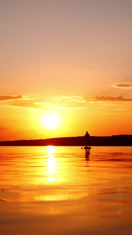 bright orange sun reflects in the river at sunset. lonely man oars standing on the sup board approaching camera. low angle view. vertical video.