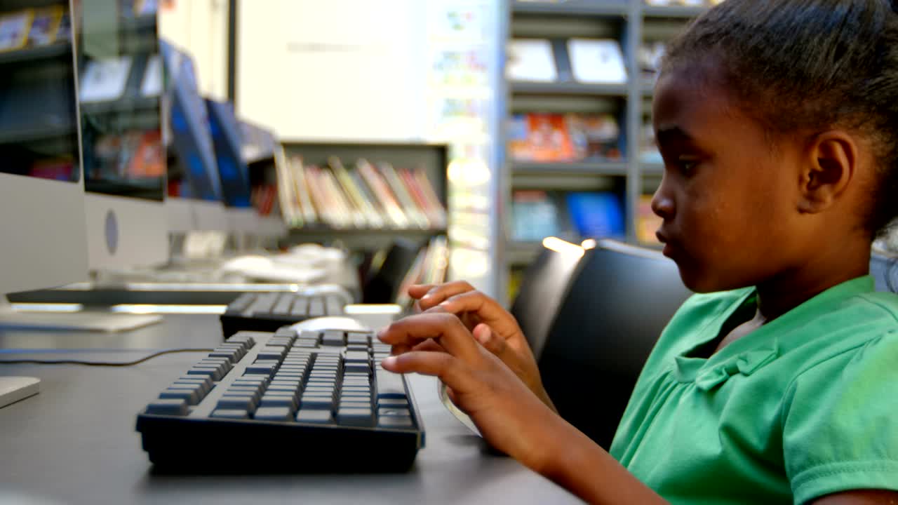 Side view of African American schoolgirl using computer in library at school 4k