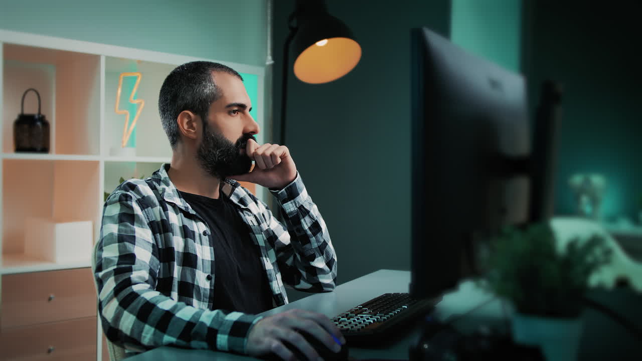 Handsome Caucasian man sitting behind his desk working on a project at his cool home office with a lightning bolt neon sign and teal and orange lights in the background