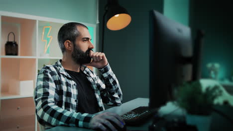 Schöner-Kaukasischer-Mann,-Der-Hinter-Seinem-Schreibtisch-Sitzt-Und-An-Einem-Projekt-In-Seinem-Coolen-Heimbüro-Arbeitet,-Mit-Einem-Blitz-Neonschild-Und-Blaugrünen-Und-Orangefarbenen-Lichtern-Im-Hintergrund