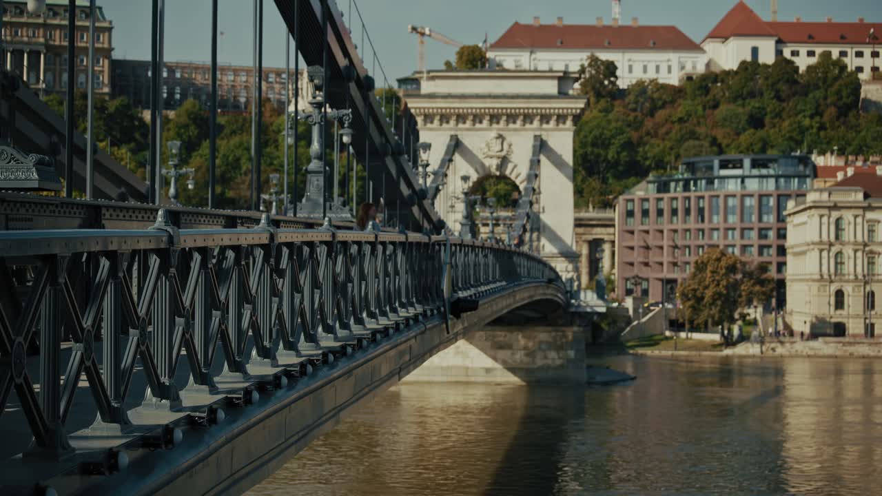 Chain Bridge in Budapest with intricate railing details, a person walking, and city buildings