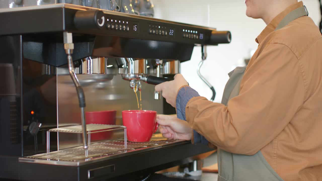 Barista bionda che blocca il portafiltro mentre prepara un caffè espresso in una tazza rossa al bancone di un bar e saluta