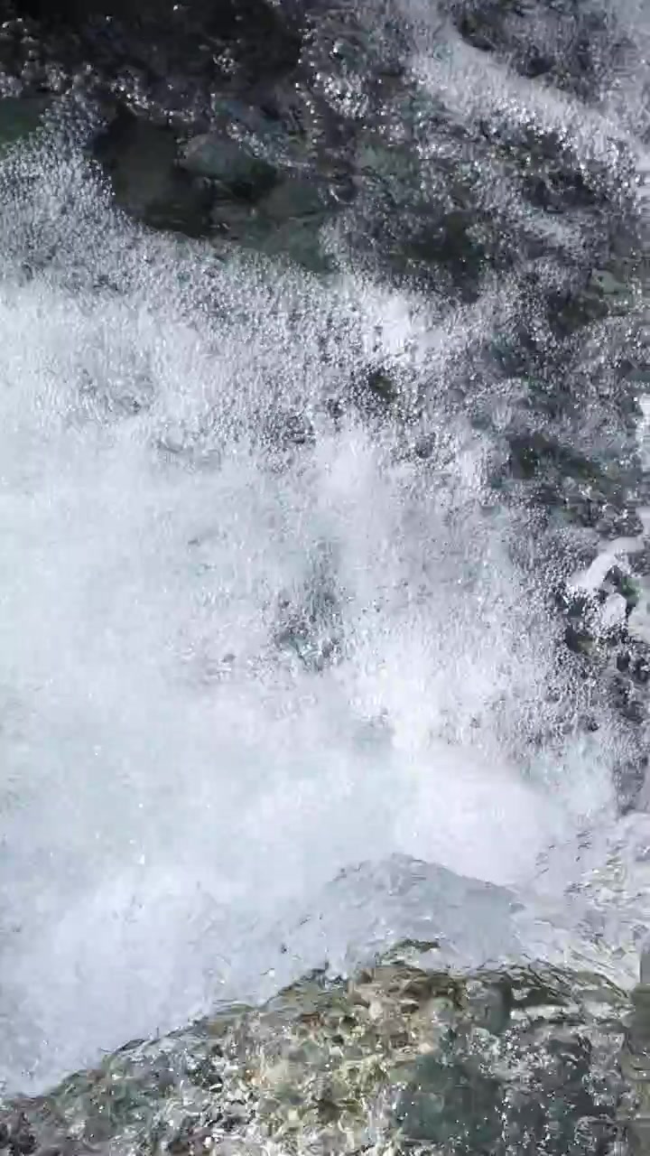 Clear mountain stream water rushes energetically over jagged rocks in daylight, captured from above with a steady camera for a dynamic, natural scene