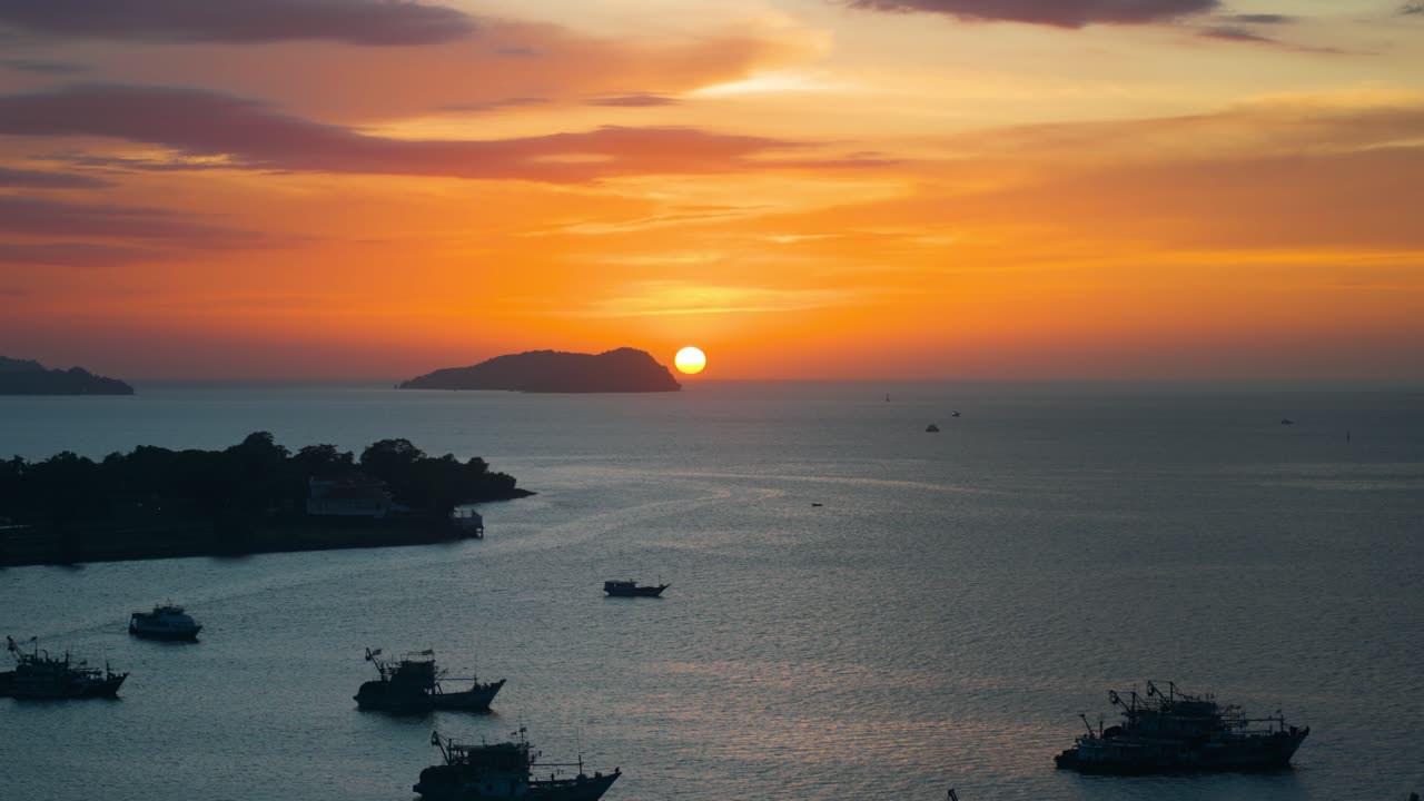 Breathtaking aerial view of the sun setting over the sea and distant islands at Kota Kinabalu Waterfront harbour filled with silhouetted fishing boats in Sabah Malaysia