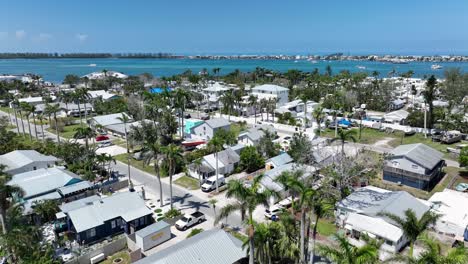 tropical housing area with river bay view in cortez, florida. palm trees along streets and garden. white houses with grey roofs. aerial flyover wide shot. cruising boats in distance.