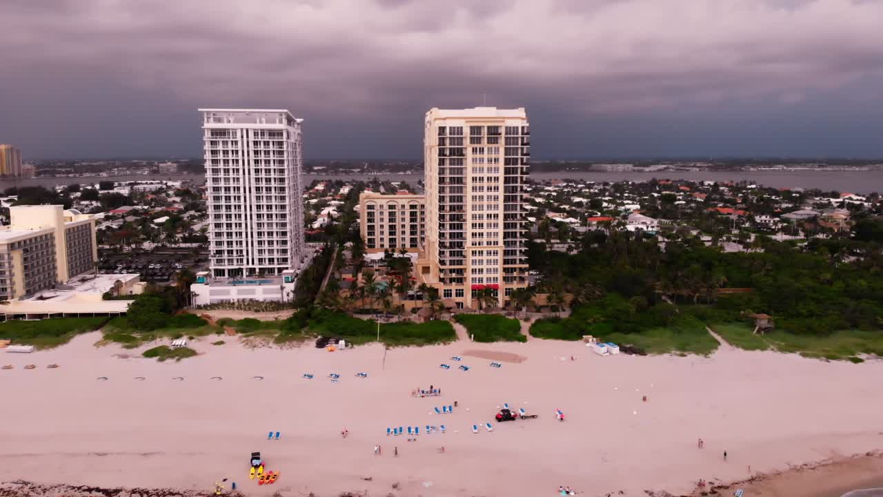 A drone shot with a jib-down motion descends over the ocean near a coastal city at sunrise, capturing waves and the horizon under a golden sky.