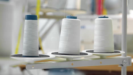 primer plano de tres grandes bobinas con hilo blanco delgado en una máquina de coser profesional en funcionamiento. imágenes de video en tiempo real en alta definición