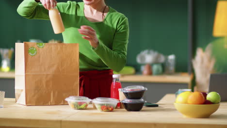 mujer descargando alimentos y bebidas ecológicas de una bolsa de papel en casa