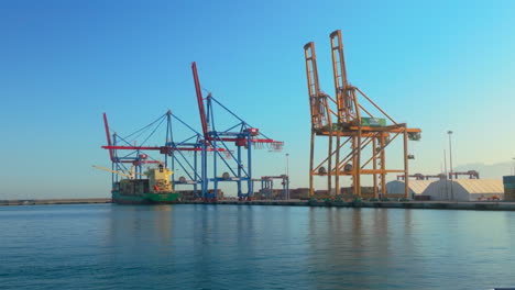 a view of the malaga port, featuring large industrial cranes along the waterfront, with a container ship docked under a clear blue sky