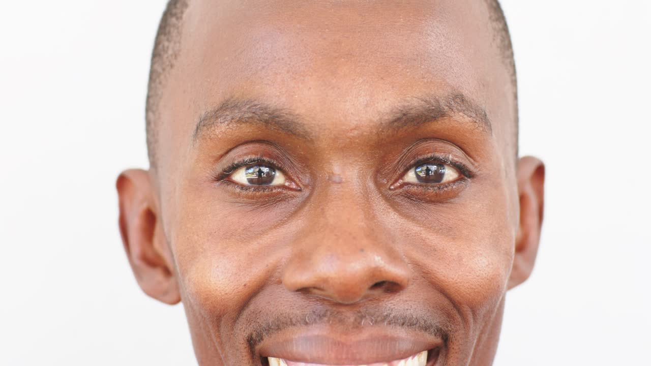 African man holding camera gaze on white backdrop, shifting to broad laughing smile and blinking