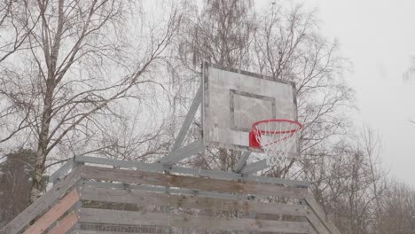 Low-angle-shot-of-snow-falling-on-forest-mounted-basketball-hoop-on-a-cold-winter-day