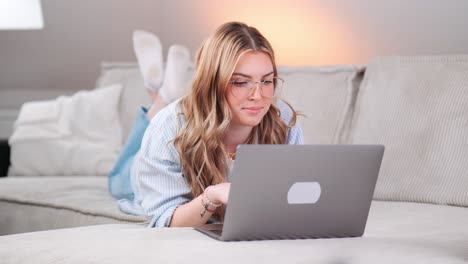 a young beautiful woman lies on the sofa and surfs on her notebook