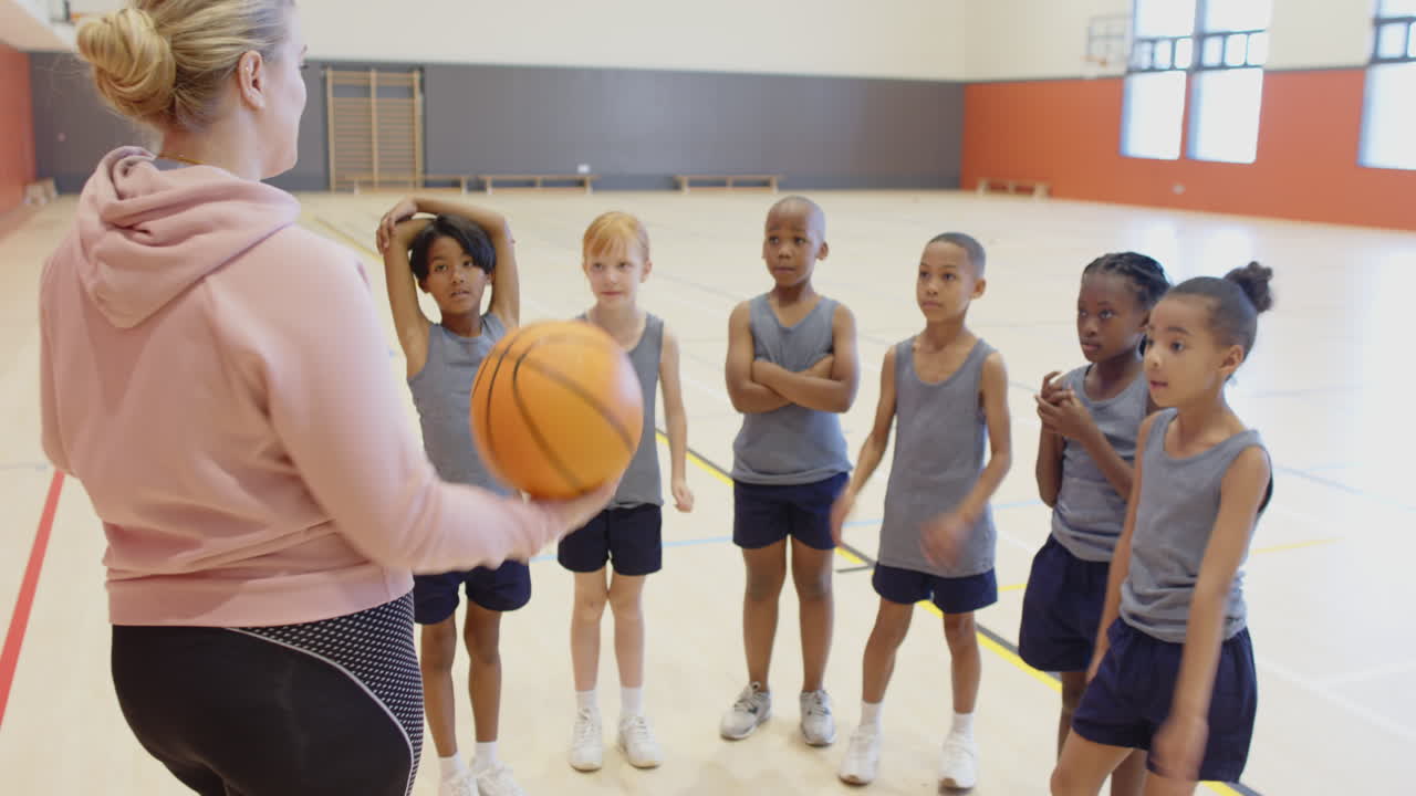 In de schoolgymzaal begeleidt een coach kinderen die basketballen, genietend van teamwork.