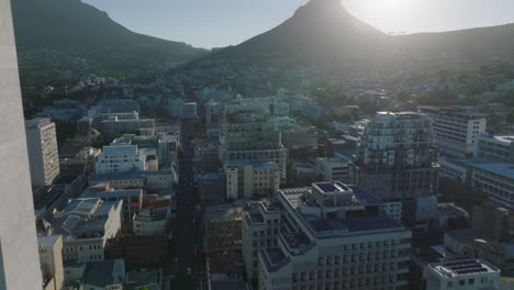 High-angle-view-of-town-development.-Tilt-up-reveal-of-Lions-Head-mountain-casting-shadow-on-buildings-in-urban-neighbourhood.-Cape-Town,-South-Africa