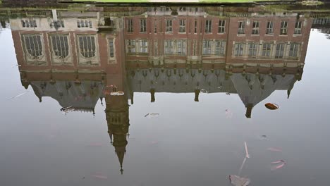 Vista-Del-Palacio-De-La-Paz,-Vredespaleis-En-Holandés,-Reflejada-En-El-Estanque-Del-Jardín-Bajo-Un-Cielo-Opaco.