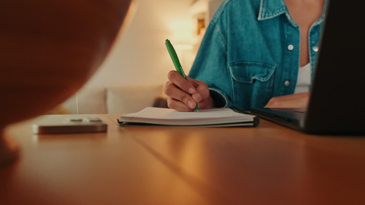 Close-Up of a Person's Hand Writing Notes in a Notebook at a Desk