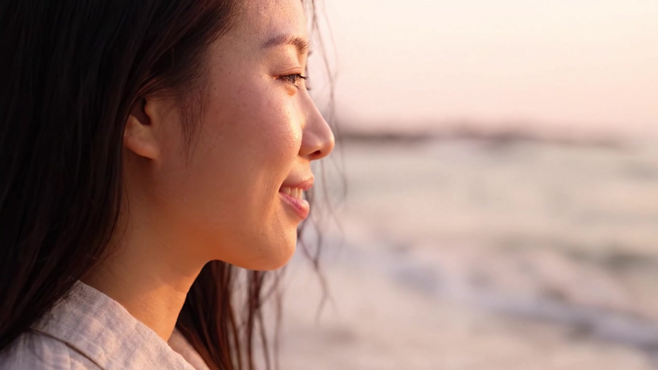 海辺での瞑想的なひととき：目を閉じて自然の穏やかな美しさを満喫する女性。夕暮れ時に平和と静けさを抱きしめています。